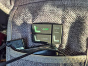 Drei schwarze rechteckige Tasten auf grauem Stoff, zwei zeigen grüne Beschriftungen 'Upper' und 'Lower' mit Sitz-Piktogrammen; ein schwarzes Kabel liegt darüber