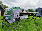 Tenda a cupola verde, due sedie pieghevoli e un tavolo da campeggio con tazze e stoviglie sull'erba, cielo nuvoloso