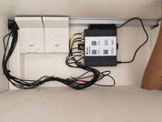 Interior de un armario con dos cajas rectangulares blancas a la izquierda, una con la etiqueta "12V", un dispositivo rectangular negro a la derecha con varios cables conectados, muchos cables negros a lo largo de la parte inferior, cartón marrón en la pared interior derecha