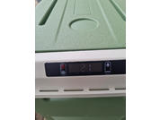 Couvercle en plastique vert texturé avec une empreinte ronde; en dessous, un panneau blanc avec un affichage numérique noir indiquant '21' et deux boutons avec symbole plus et marche/arrêt; fentes de ventilation et boîtier vert en dessous