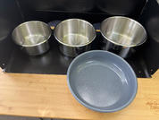 Three stainless steel bowls lined up on a black shelf; in front, a round gray-blue bowl on a wooden countertop