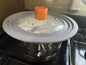 Stainless steel pot on stovetop with glass lid, gray silicone rim and orange knob