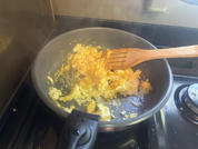 Scrambled eggs in a frying pan on a stove with a wooden spatula