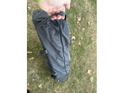 Main tenant la poignée d'un sac gris foncé posé sur de l'herbe avec des feuilles sèches