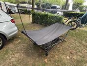 Toile noire tendue sur une structure métallique pliante sur la pelouse; à gauche une voiture argentée, à l'arrière un vélo, une haie et des arbres