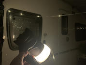 Mano che tiene una torcia che illumina il vetro di una porta di caravan/rimorchio; piccole luci si riflettono sul vetro