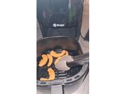 Interior of a black air fryer with the basket open, several orange-golden curved pieces inside, a black tong holding one piece; device logo "Berger" visible