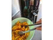 Green bowl with seasoned potato wedges, metal tongs holding a wedge, black air fryer in the background