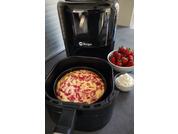 Black air fryer with a cake showing red swirls in the basket, next to a bowl of strawberries and a bowl of white cream on a gray countertop