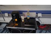 Black countertop with a black appliance with display and handle, a drink carton, a plastic bottle with yellow cap, a flat black cooktop, two white wall sockets, and a red cable reel