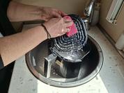 Due avambracci e mani tengono una spugna rosa e strofinano una padella grill nera con schiuma di sapone sopra un lavabo rotondo accanto a un rubinetto