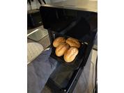 Forno aperto con una teglia contenente cinque panini dorati; una mano con un guanto da forno blu tiene la teglia