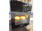 Forno da tavolo nero con portina in vetro, due panini rotondi su una griglia all'interno; a destra panini confezionati in plastica; logo 'Berger' sotto la porta