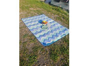 Rectangular mat with blue and white chevron stripes on grass and gravel, with a bowl of fruit and two plates on it