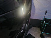 Schwarzes Fahrzeug seitlich mit sichtbarem Rad; stabförmige Lampe zwischen Fahrzeug und Zelt; Zeltinnenwand, grauer Bodenbelag und zusammenklappbarer Stuhl mit türkisfarbenen Kanten