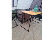 Interieur van een tent met een opvouwbare houten tafel, een groene thermosfles op de tafel, een opvouwbare stoel links en een grijze stoffen opbergbox onder de tafel