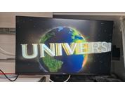 Écran plat affiche de grandes lettres dorées 'UNIVERSAL' devant une image de la Terre sur un fond étoilé sombre