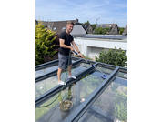 Homme debout sur un toit en verre avec des maisons et des arbres en arrière-plan par jour ensoleillé