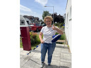 Garçon portant un t-shirt bleu et un jean debout à côté d'une boîte aux lettres rouge sur un trottoir avec des maisons en arrière-plan