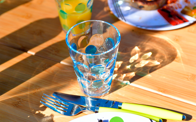 Glass of water and cutlery on a wooden table in sunlight
