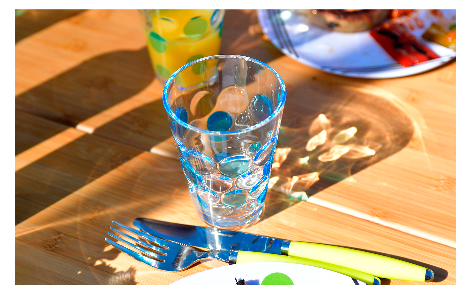 Glass of water and cutlery on a wooden table in sunlight