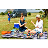 Drei Frauen beim Picknick auf einer Decke auf einer Wiese mit einem Camper im Hintergrund