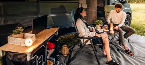 Groupe de jeunes assis à une table de camping devant deux camping-cars au coucher du soleil