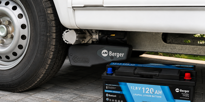 Wei&szlig;e Fahrzeugseite mit Stahlrad; darunter ein schwarzer Wagenheber mit Berger-Logo und daneben eine schwarz-blaue 12,8V 120 Ah Lithium-Batterie auf Pflastersteinen