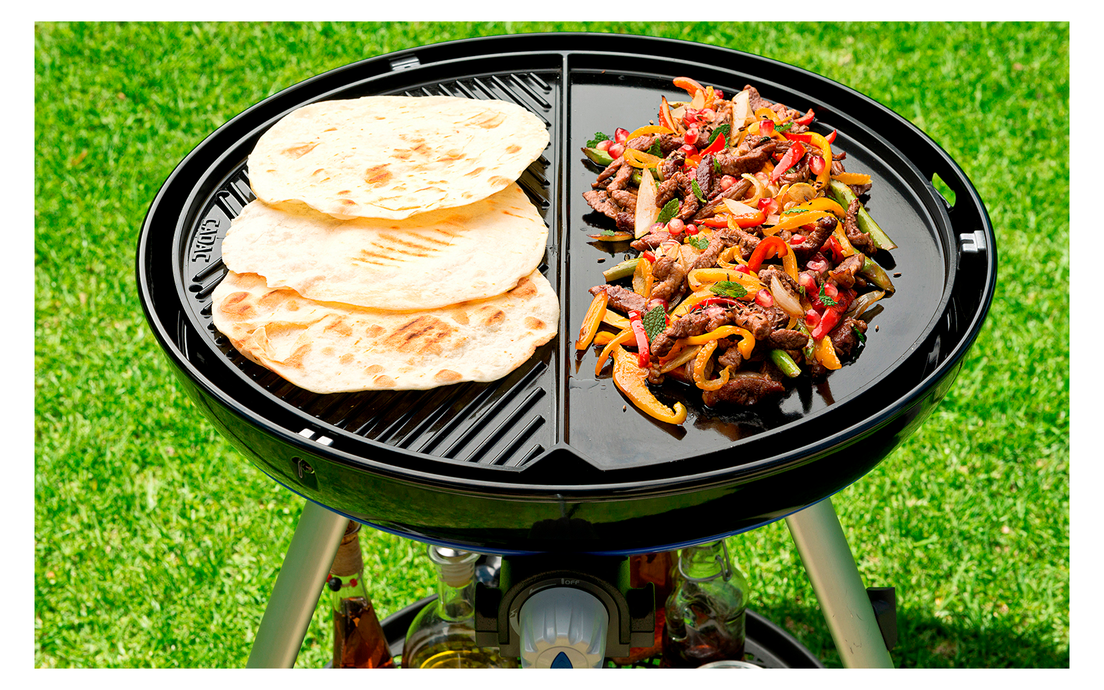 Grill mit Fleisch und Fladenbrot auf Rasen