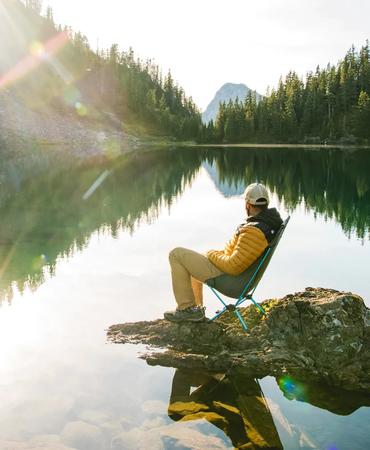 Person sitting on a chair by a mountain lake